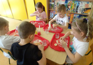 Dzieci mieszają składniki na ciastolinę na tackach rozłożonych przed każdym dzieckiem na stole.
